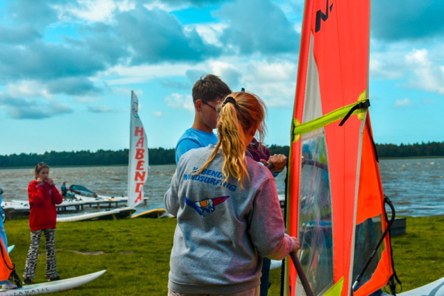 Dwie osoby z deską windsurfingową, przygotowania do pływania – spojrzenie na jezioro.