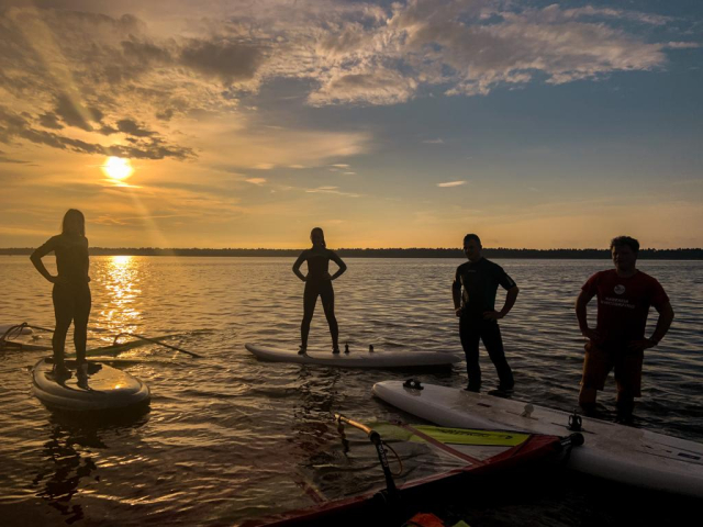 Nauka windsurfingu w jeziorze przy zachodzącym słońcu – instruktorzy i uczniowie w wodzie.
