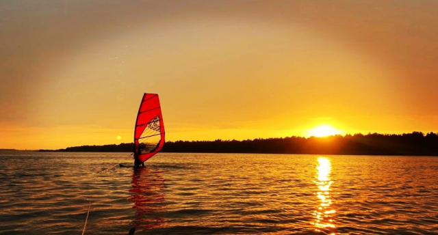 Pływanie na desce windsurfingowej o złotej godzinie – słońce nad taflą jeziora.